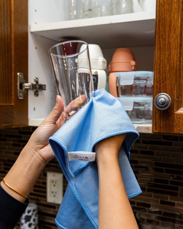 LīQ Home microfiber glass cleaning cloth wiping a clear drinking glass in kitchen cabinet area